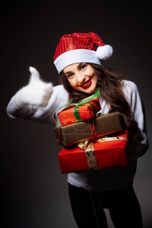 Téléchargez les photos : Une femme tient une pile de cadeaux et donne un pouce vers le haut. Concept de joie et d'excitation - en image libre de droit