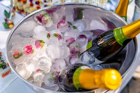 Téléchargez les photos : Un bol de glace rempli de champagne et de fleurs. Le champagne est en deux bouteilles, dont une en or - en image libre de droit