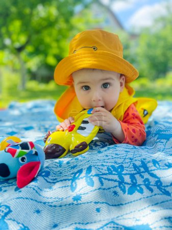 Téléchargez les photos : A baby wearing a yellow hat and a yellow jacket laying on a blanket. The baby has a serious expression on its face - en image libre de droit