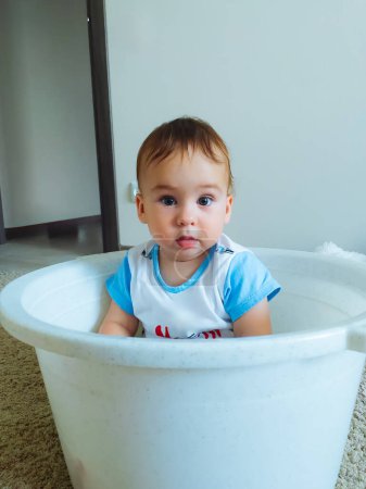 Téléchargez les photos : A baby is sitting in a white bucket. The baby is wearing a blue shirt - en image libre de droit