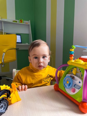 Téléchargez les photos : A baby is sitting at a table with a toy truck and a toy car. The baby is wearing a yellow shirt and he is looking at the toys - en image libre de droit