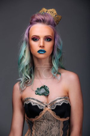 Téléchargez les photos : A woman with purple and blue hair is wearing a crown and a necklace. She is standing in front of a gray background - en image libre de droit