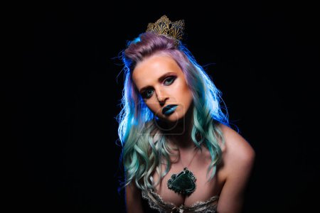 Téléchargez les photos : A woman with long green hair and blue lips is wearing a crown and a necklace. She is standing in front of a black background - en image libre de droit