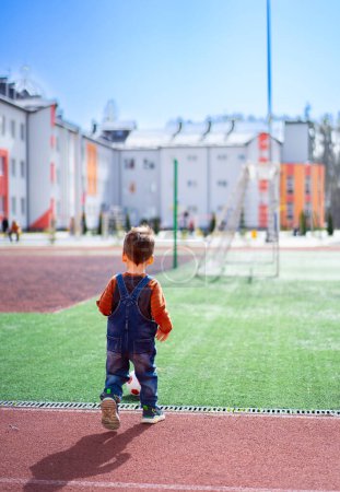 Téléchargez les photos : A young boy is walking on a field with a soccer ball in his hand. - en image libre de droit
