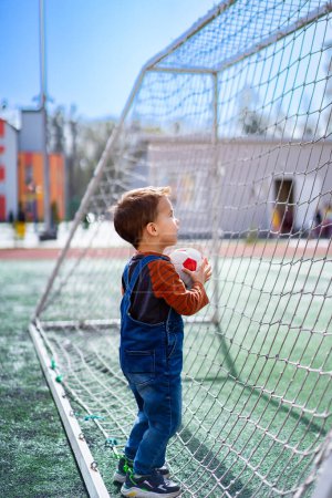 Photo for A young boy is holding a soccer ball and looking at the goal. Concept of excitement and anticipation for the game to begin - Royalty Free Image