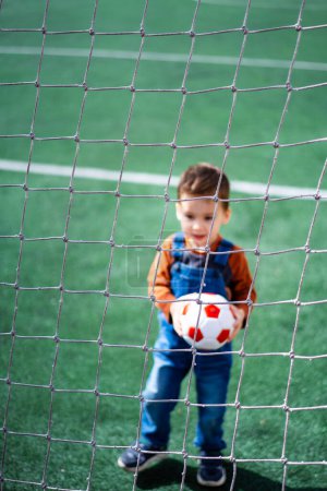Téléchargez les photos : A young boy is holding a soccer ball in front of a net. The boy is smiling and he is enjoying himself - en image libre de droit