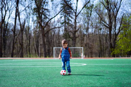 Téléchargez les photos : A young boy is playing soccer on a field. He is wearing a red shirt and blue overalls - en image libre de droit