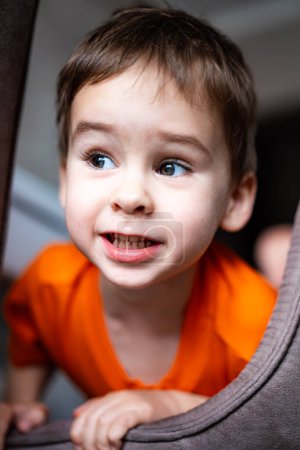 Téléchargez les photos : Un jeune garçon en chemise orange regarde la caméra avec un sourire sur le visage. Il a une brosse à dents dans la bouche et porte une chemise avec un visage souriant dessus - en image libre de droit