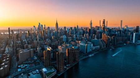 Téléchargez les photos : Lumière orange du soleil couchant illuminant les gratte-ciel et les immeubles de grande hauteur du paysage new-yorkais. Vue de dessus sur la métropole depuis l'East River. - en image libre de droit