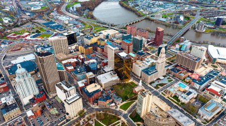 Photo for Downtown of beautiful modern Hartford, Connecticut, the USA at daytime. View on the river floating through the city at backdrop. Aerial perspective. - Royalty Free Image