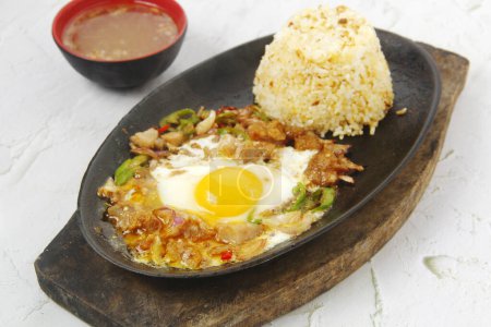 Foto von frisch gekochtem philippinischem Essen namens Sizzling Sisig oder gehackter Schweinehaut, serviert mit gebratenem Reis.