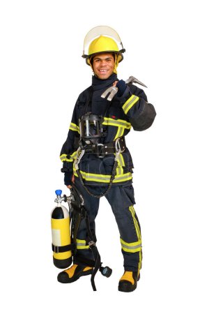 Joven hombre afroamericano sonriente de cuerpo completo en uniforme de bombero con aparato de cilindro de aire respirable y respirador de cara completa y palanca hooligan en la mano, aislado sobre fondo blanco
