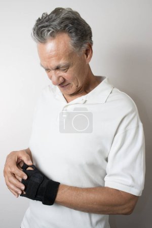 Foto de Hombre mayor con un brazalete en la mano izquierda y la muñeca para controlar el dolor - Imagen libre de derechos