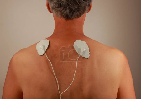 Mann mit Elektrotherapie-Massagegerät oder Zehner-Einheit auf dem Rücken