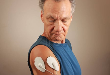 Man using an Electro Therapy Massager or Tens Unit on his Deltoid for pain relief for Muscles and Joints 