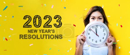Téléchargez les photos : 2023 Résolutions du Nouvel An avec une jeune femme tenant une horloge montrant près de 12 - en image libre de droit