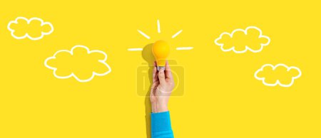 Photo for Person holding a yellow light bulb with cloud sketches - Royalty Free Image