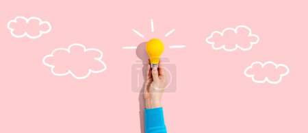 Photo for Person holding a yellow light bulb with cloud sketches - Royalty Free Image