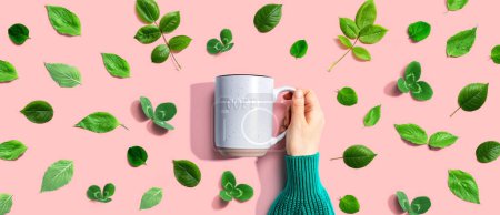 Photo for Person holding a mug with green leaves - flat lay - Royalty Free Image