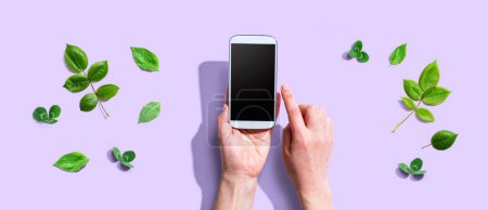 Photo for Person using a smartphone with green leaves - flat lay - Royalty Free Image