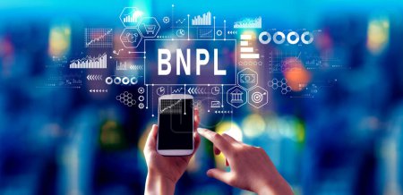 Foto de BNPL - Comprar ahora Pay Later theme with person using a smartphone in a city at night - Imagen libre de derechos