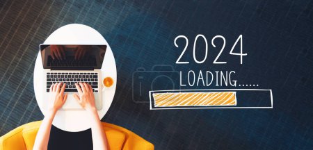 Téléchargez les photos : Chargement du nouvel an 2024 avec personne utilisant un ordinateur portable sur une table blanche - en image libre de droit