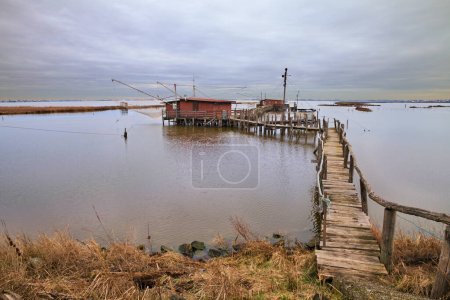 Photo for Comacchio, Ferrara, Emilia Romagna, Italy: landscape of the wetland in the nature reserve Po Delta Park with fishing huts in the lagoon - Royalty Free Image