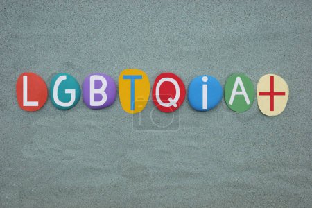 LGBTQIA Plus, creative logo composed with hand painted multi colored stone letters over green sand