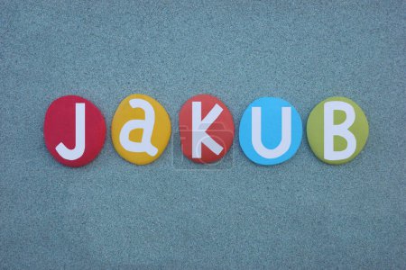 Jakub, masculine given name composed with hand painted multi colored stone letters over green sand