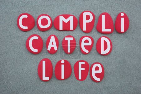 Complicated life, real thought composed with hand painted red colored stone letters over green sand