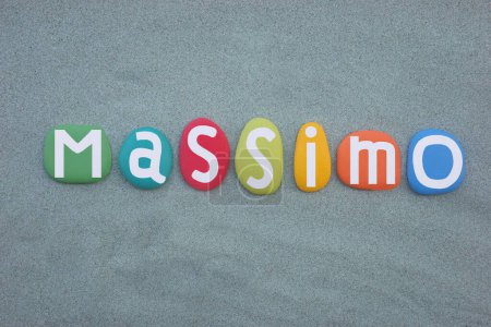 Feier von Massimo, männlicher italienischer Vorname bestehend aus handbemalten mehrfarbigen Steinbuchstaben über grünem Sand