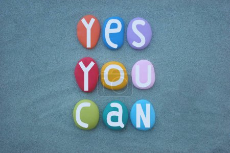 Yes, you can, creative and motivational slogan composed with hand painted multi colored stone letters over green sand