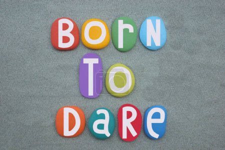 Born to dare, creative text composed with hand painted multi colored stone letters over green sand