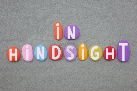 Hindsight is the ability to understand and realize something about an event after it has happened, creative text composed with hand painted multi colored stone letters over green sand