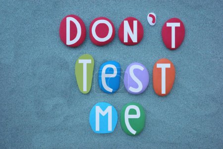 Do not test me, advice message composed with multi colored stone letters over green sand