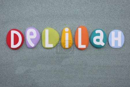 Delilah, feminine given name composed with hand painted multi colored stone letters over green sand