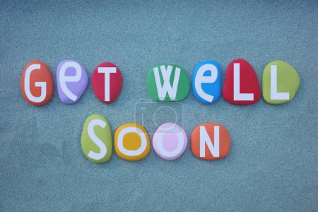 Get well soon, message of encouragement composed with hand painted multi colored stone letters over green sand