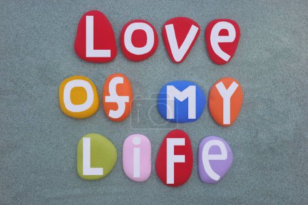 Liebe meines Lebens, kreative Liebesbotschaft komponiert mit künstlerisch handgemalten mehrfarbigen Steinbuchstaben über grünem Sand