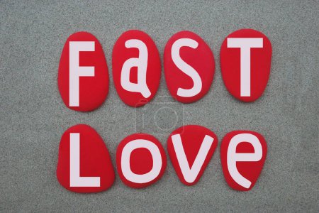 Fast love, creative text composed with hand painted red colored stone letters over green sand