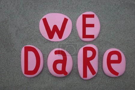 Photo for We dare, creative slogan composed with hand painted pink and red colored stone letters over green sand - Royalty Free Image