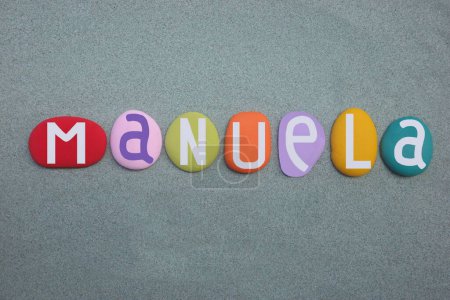 Manuela, nombre femenino compuesto por letras de piedra multicolor pintadas a mano sobre arena verde