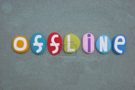 Offline, creative text composed with hand painted multi colored stone letters over green sand