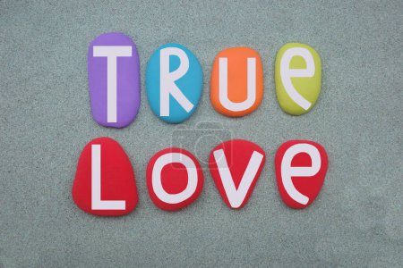 True love, creative text composed with multi colored stone letters over green sand