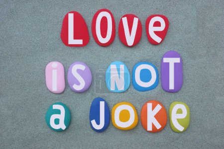 Love is not a joke, creative slogan composed with multi colored stone letters over green sand