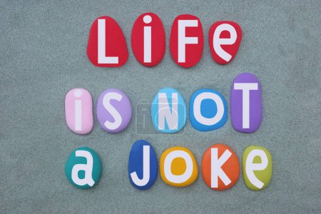 Life is not a joke, creative slogan composed with multi colored stone letters over green sand