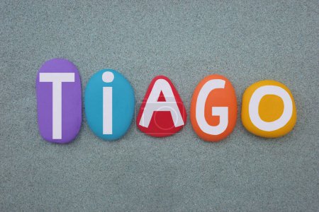 Tiago, masculine given name composed with hand painted multi colored stone letters over green sand