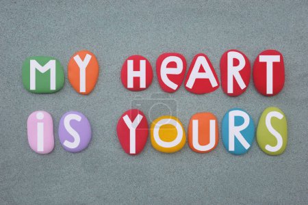 My heart is yours, creative love message composed with multi colored stone letters over green sand