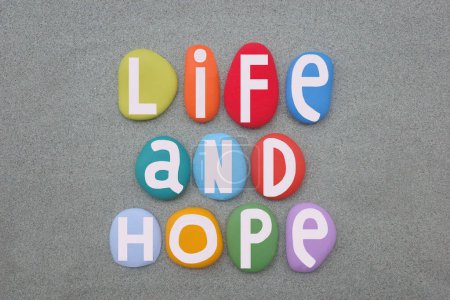 Life and hope, creative slogan composed with hand painted multi colored stone letters over green sand