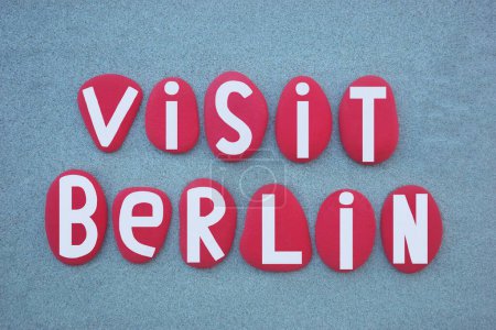 Visit Berlin, creative logo composed with hand painted red colored stone letters over green sand