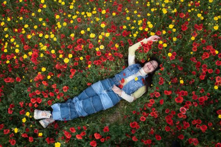Young happy girl resting in the field of red poppy flowers. Drone aerial of woman in spring
